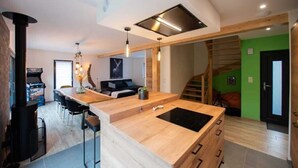 A modern kitchen with a central island, bar stools, a built-in stove, and a staircase leading to a green room. - 
Maéva's Chalet: Jacuzzi and Terrace. (Xonrupt-Longemer)