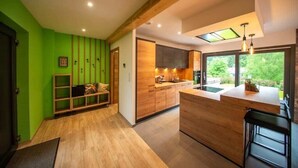 A modern kitchen with wooden cabinets, a central island, and a view of greenery outside. - 
Maéva's Chalet: Jacuzzi and Terrace. (Xonrupt-Longemer)