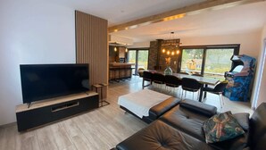 A modern living room with a flat-screen TV, a sofa, a dining area, and a kitchen visible through an open space. - 
Maéva's Chalet: Jacuzzi and Terrace. (Xonrupt-Longemer)