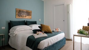 A neatly made bed with white and teal bedding, a brown pillow, and a small table with towels and flowers. - Magic Home Turin  (Torino)