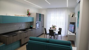 A modern kitchen with a built-in oven, a dining area with a table and chairs, and a teal sofa. - Magic Home Turin  (Torino)