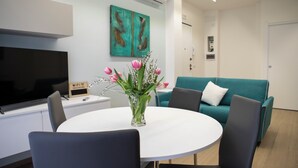 A modern living room with a white round table, black chairs, a teal sofa, and a painting on the wall. - Magic Home Turin  (Torino)