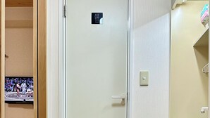 Et hotelværelse med trægulv, fjernsyn ophængt på væggen, en dør med toiletskilt og et lille bord med slippers.