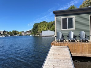 A dock extending into a calm body of water with a small house and three Adirondack chairs on the dock. - SUITE - LUXURIOUS & TRANQUIL WATERFRONT WALKOUT, WITH STUNNING VIEWS & GARDENS  (Gananoque)