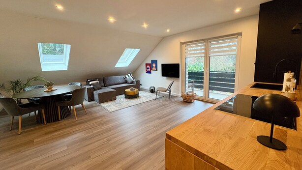 A modern living space with a dining area, a sofa, a TV, and a kitchen area.