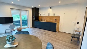 A modern kitchen with a built-in oven, a sink, and a wooden countertop. There is a dining area with a round table and blue chairs.