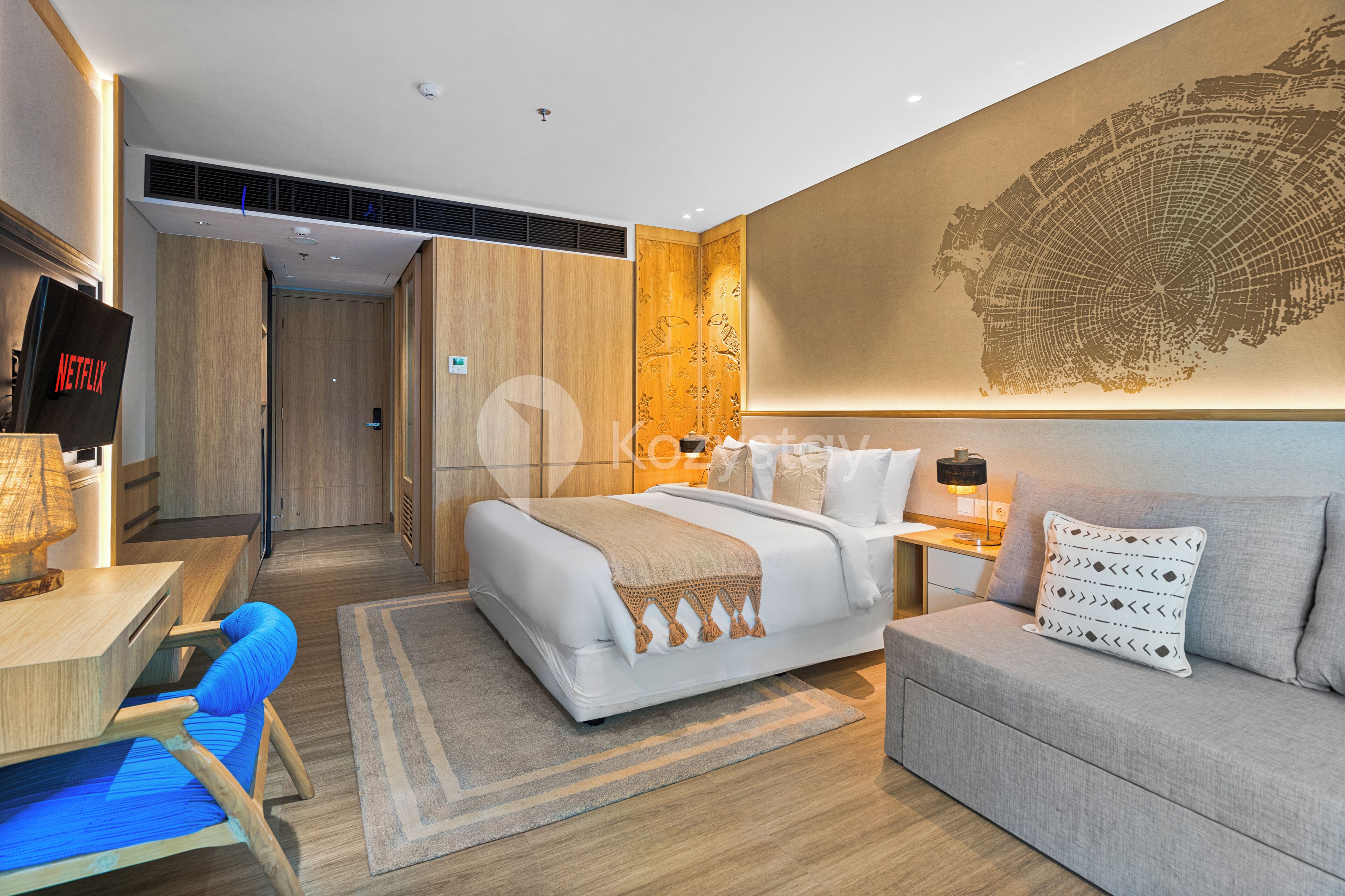 Een moderne hotelkamer met een bed, een sofa, een bureau en een aan de muur bevestigde televisie.