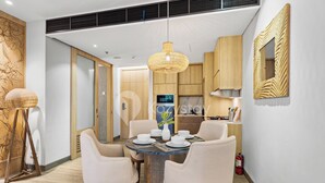 A modern dining area with a round table, six chairs, a hanging light fixture, and wooden cabinetry. - Moriya by Kozystay - Nusa Dua (Nusa Dua)