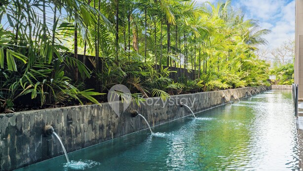 A pool with water flowing from three spouts, surrounded by lush greenery and a stone wall. - Moriya by Kozystay - Nusa Dua (Nusa Dua)