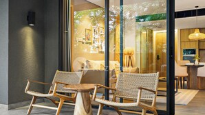 A modern interior with wicker chairs and a round table, glass doors leading to a well-lit room with a television and a plant. - Moriya by Kozystay - Nusa Dua (Nusa Dua)