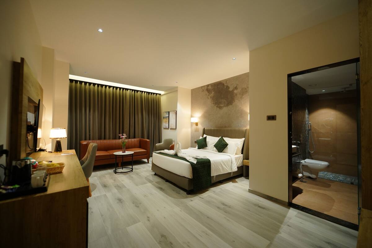 A hotel room with a bed, a sofa, a desk, and a bathroom.
