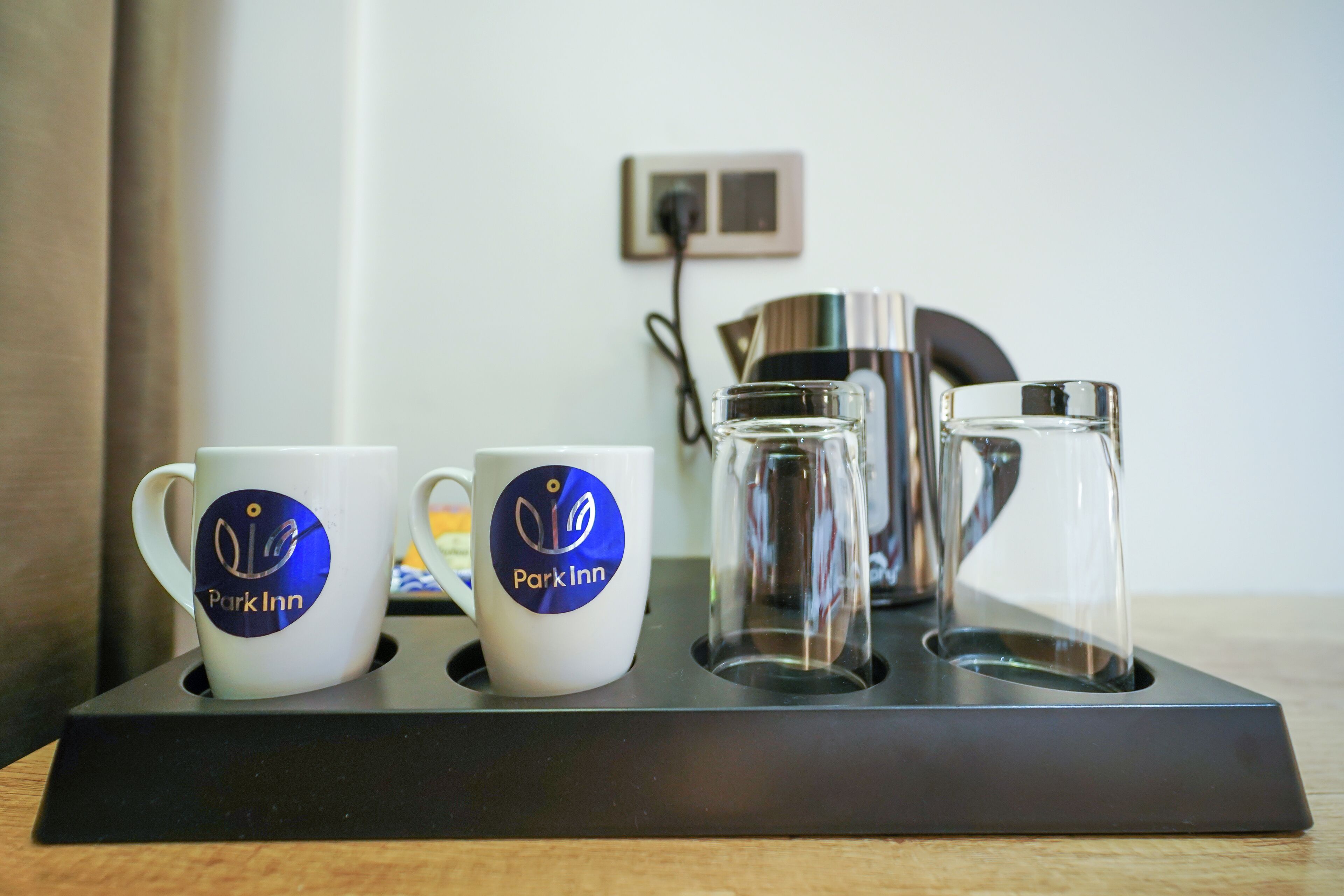 A tray with two white mugs and a glass carafe, all branded with "Park Inn" logo, on a black tray stand.