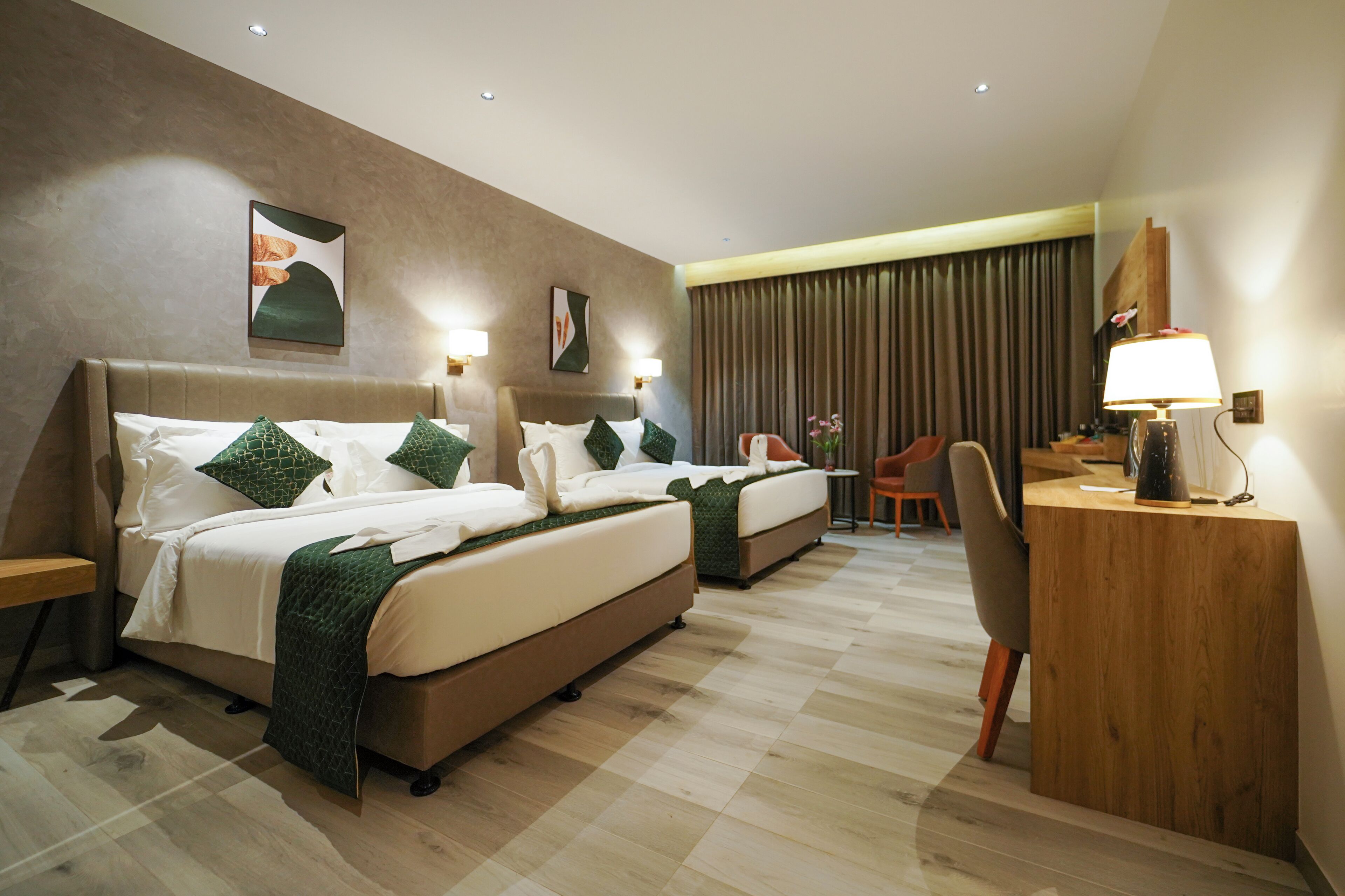 Habitación de hotel con dos camas, un escritorio, una silla y un ventanal con cortinas.