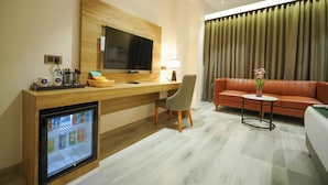 A hotel room with a wooden desk, a television, a refrigerator, a sofa, and a small table with a vase. - Hotel Park Inn Nellore - Near the Hospital & Highway (Nellore)