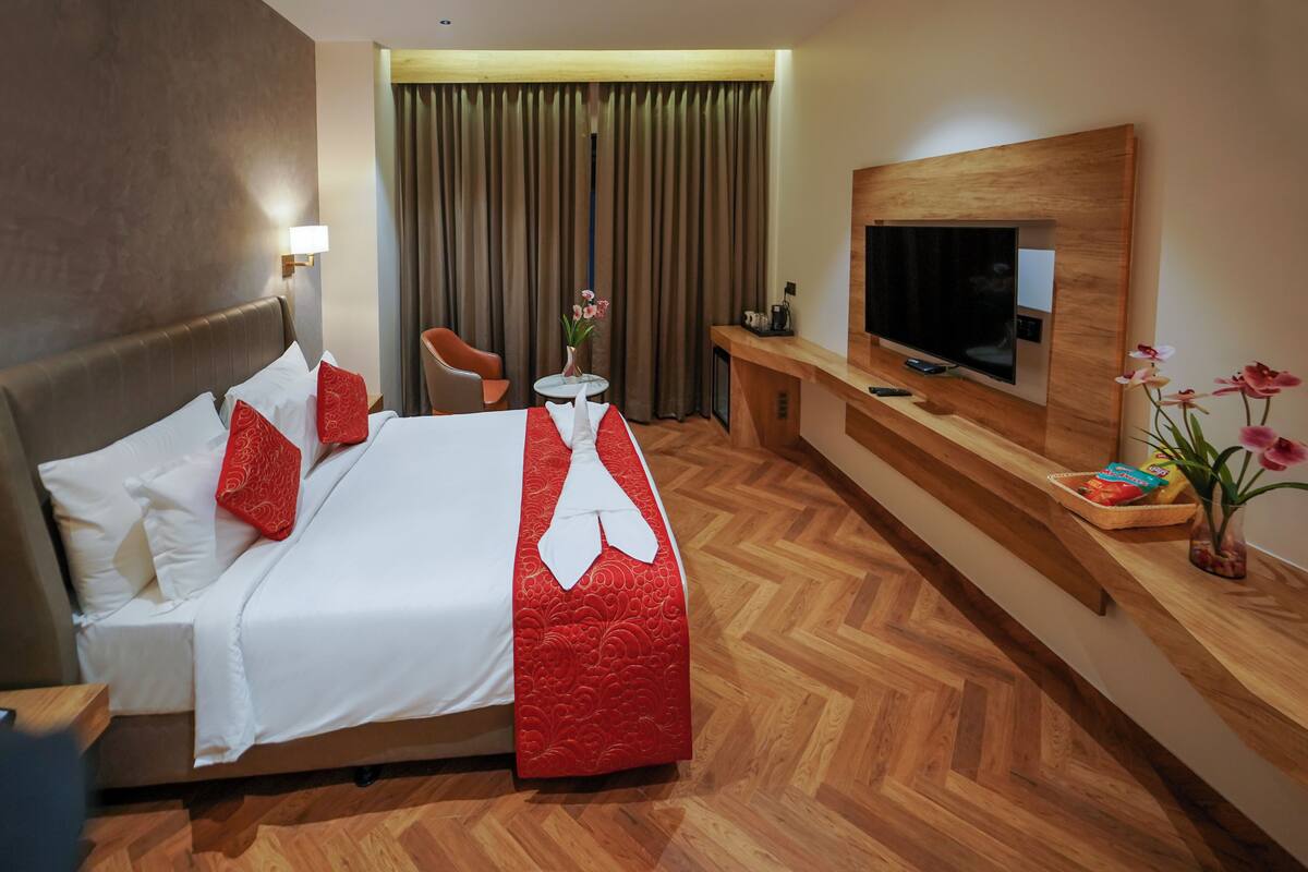 A hotel room with a large bed, a TV, a desk, and a chair.