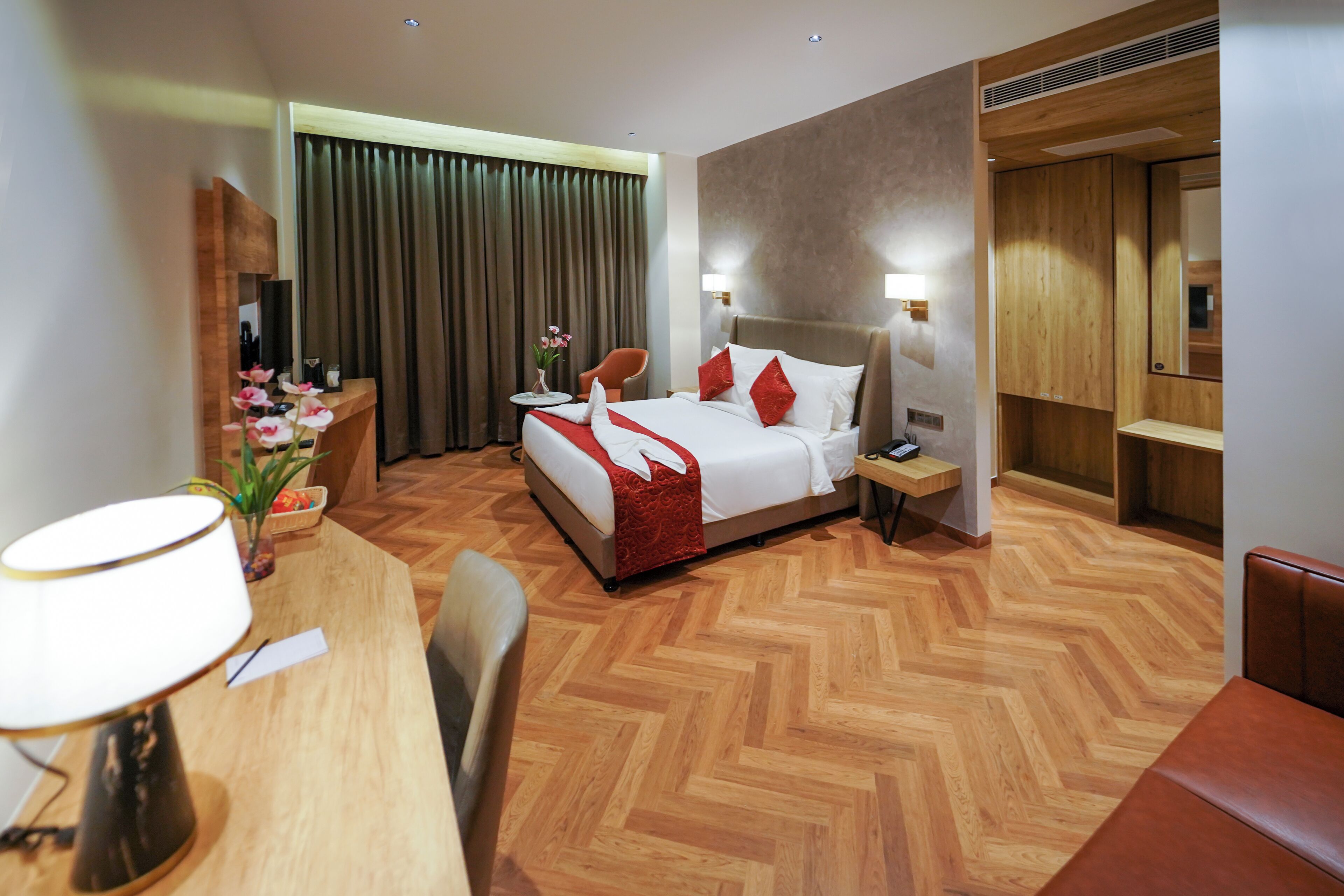 A hotel room with a bed, bedside table, lamp, chair, and a desk with a lamp.