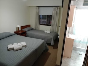 Een hotelkamer met twee bedden, een nachtkastje, een raam met gordijnen, een badkamer met een wastafel en een spiegel.
