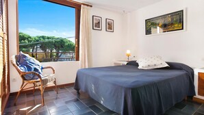 Un dormitorio con cama, una silla, una mesita de noche y una ventana con vistas a árboles y un puente.
