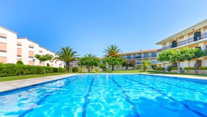 A swimming pool with clear blue water, surrounded by well-maintained greenery and buildings with balconies. - Costa Brava E-4 in Calella de Palafrugell (Palafrugell)
