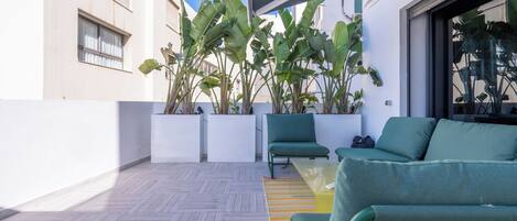 Un espace extérieur moderne, aménagé avec un canapé et des fauteuils verts, entouré de plantes en pot et doté d’un plancher en bois.
