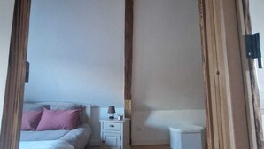 A bedroom with a bed, bedside table, nightstand, and a small white trash bin.