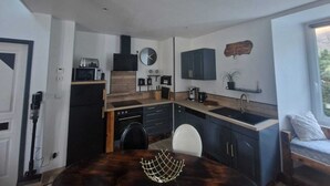 A modern kitchen with dark cabinetry, a microwave, a stove, and a sink. There is a dining table with chairs and a clock on the wall.