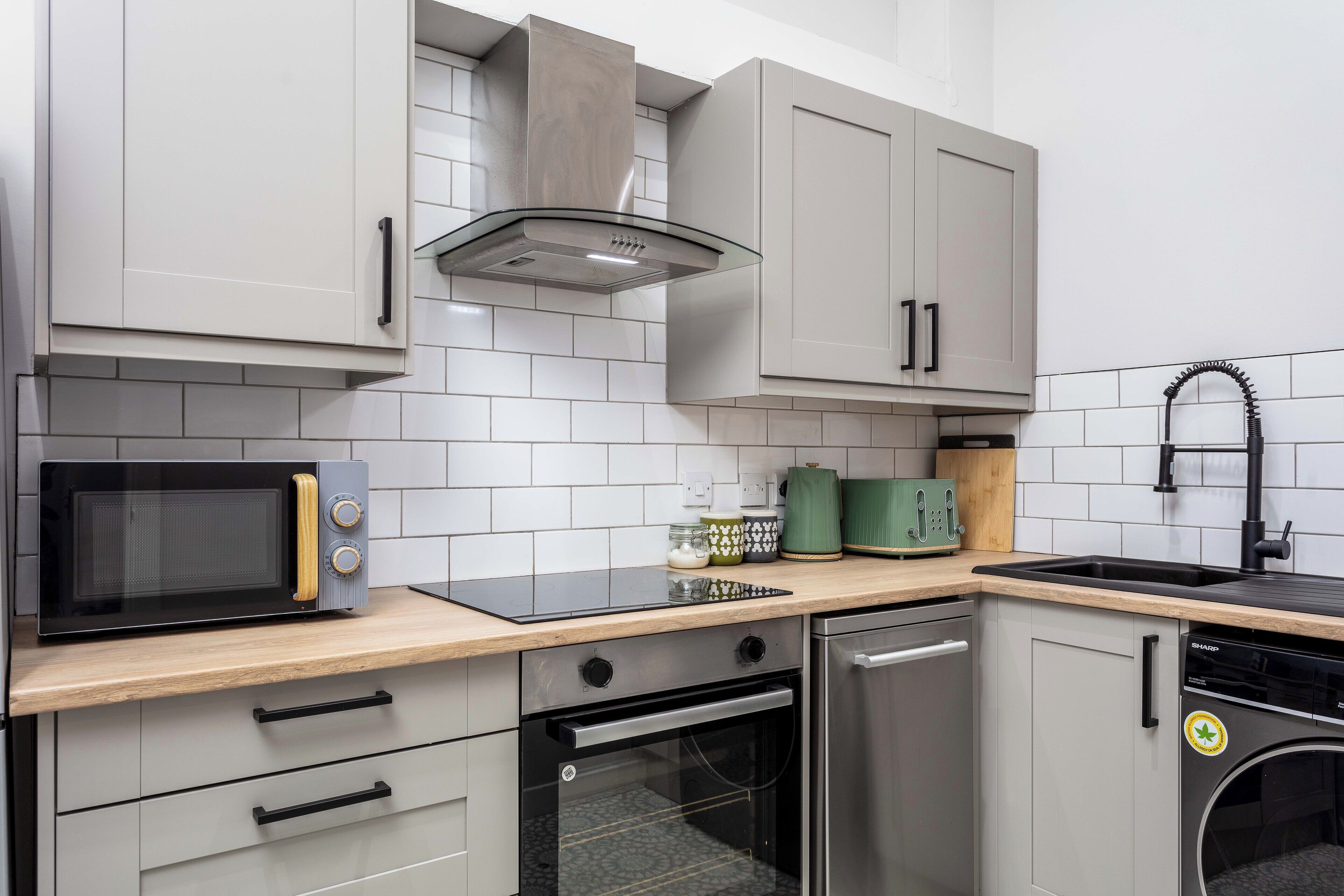 A modern kitchen with grey cabinets, a microwave, oven, dishwasher, and a sink.