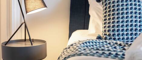 Un lit bien fait, avec une couverture à motifs et des oreillers, une lampe de sol moderne et une tête de lit sombre.