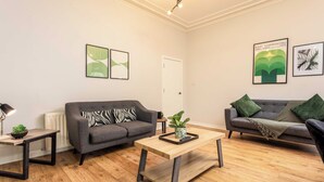 A modern living room with two grey sofas, a wooden coffee table, and a small side table with a lamp. - The Annick Suite No.1 (Irvine)