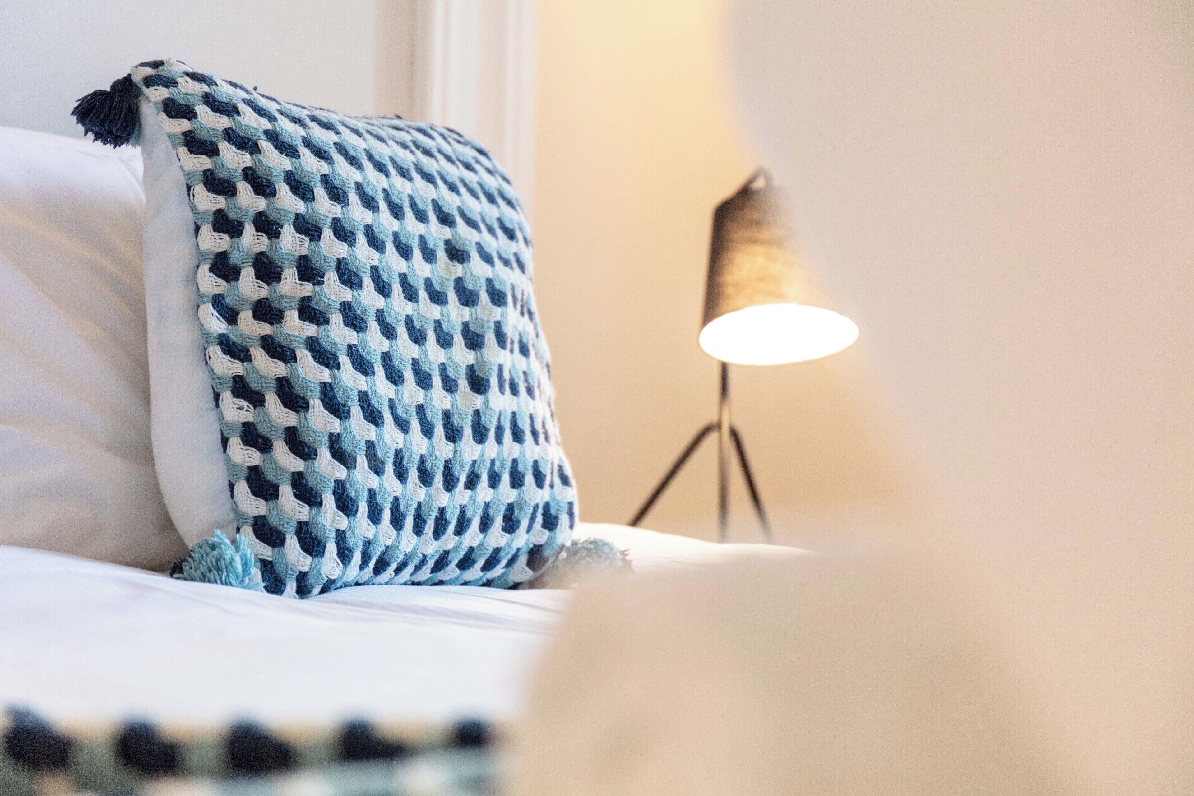 Una cama con un cojín de diseño azul y blanco y una lámpara de noche.