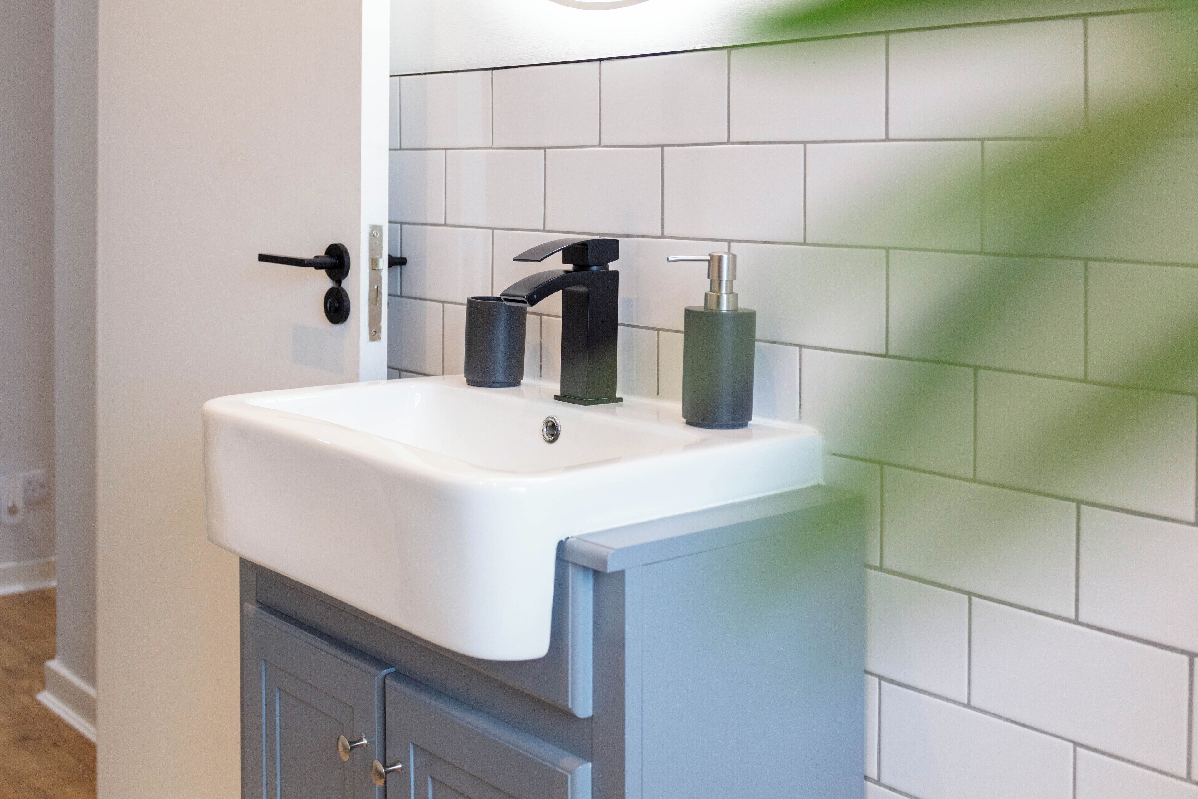 Ein Badezimmer mit einem weißen Waschbecken, einem schwarzen Wasserhahn und einem Seifenspender auf der Ablagefläche.