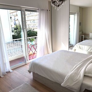 Et soveværelse med en stor seng, en balkon med gelænder og udsigt til bygninger.