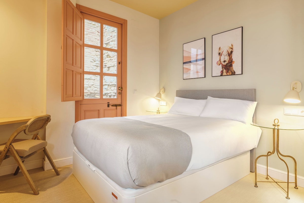 A neatly arranged hotel room with a bed, a desk, a chair, and a window with a view.