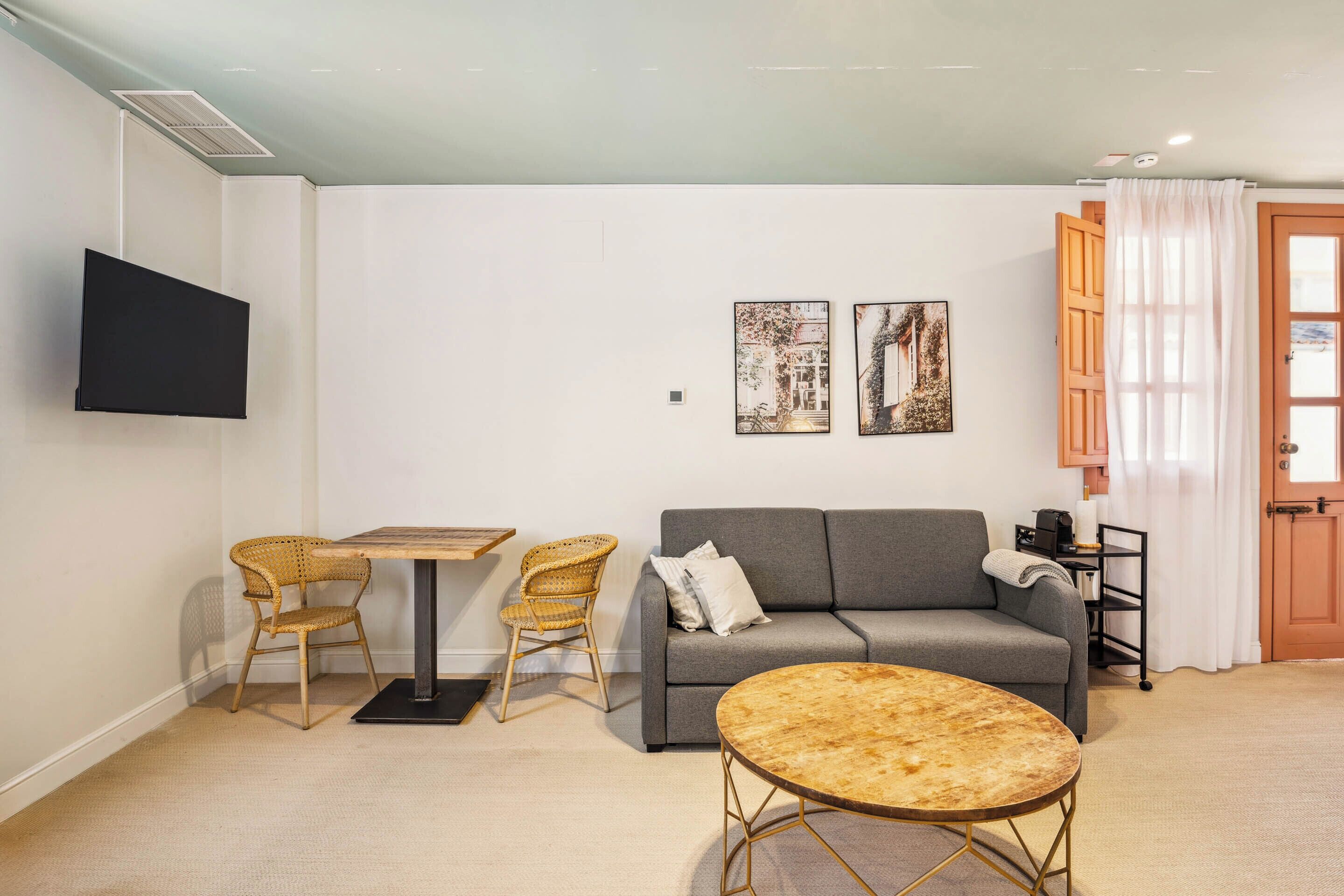 Un salon comprenant un canapé, deux fauteuils en osier, une table basse ronde et un téléviseur à écran plat fixé au mur.