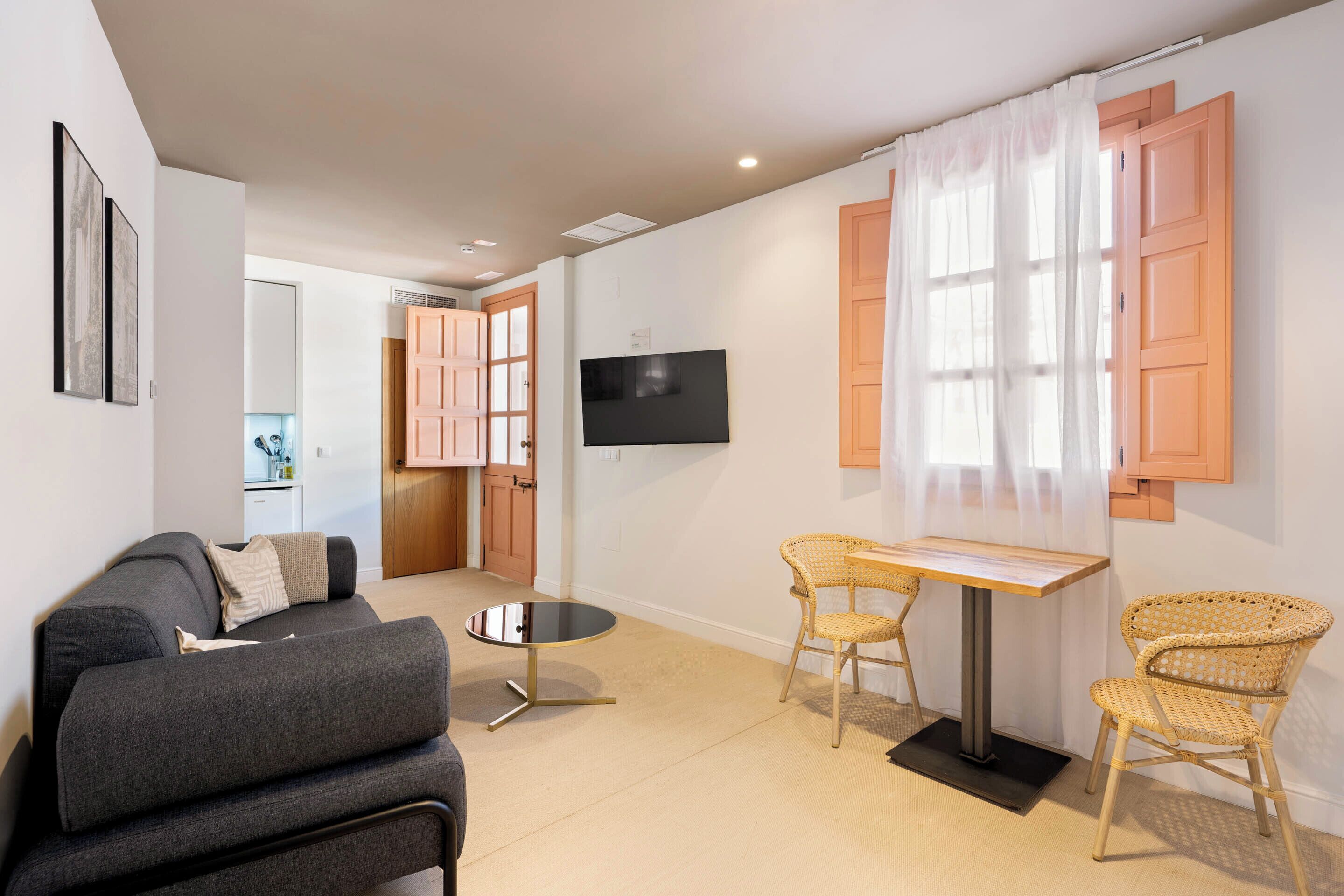 Una sala de estar moderna con un sofá, dos sillones de mimbre, una mesita y un televisor montado en la pared.