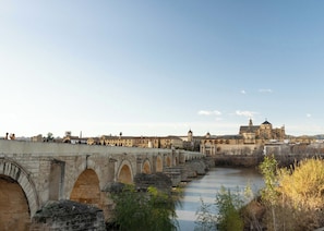 A stone bridge with arches over a river, leading to a historic building with domes.
