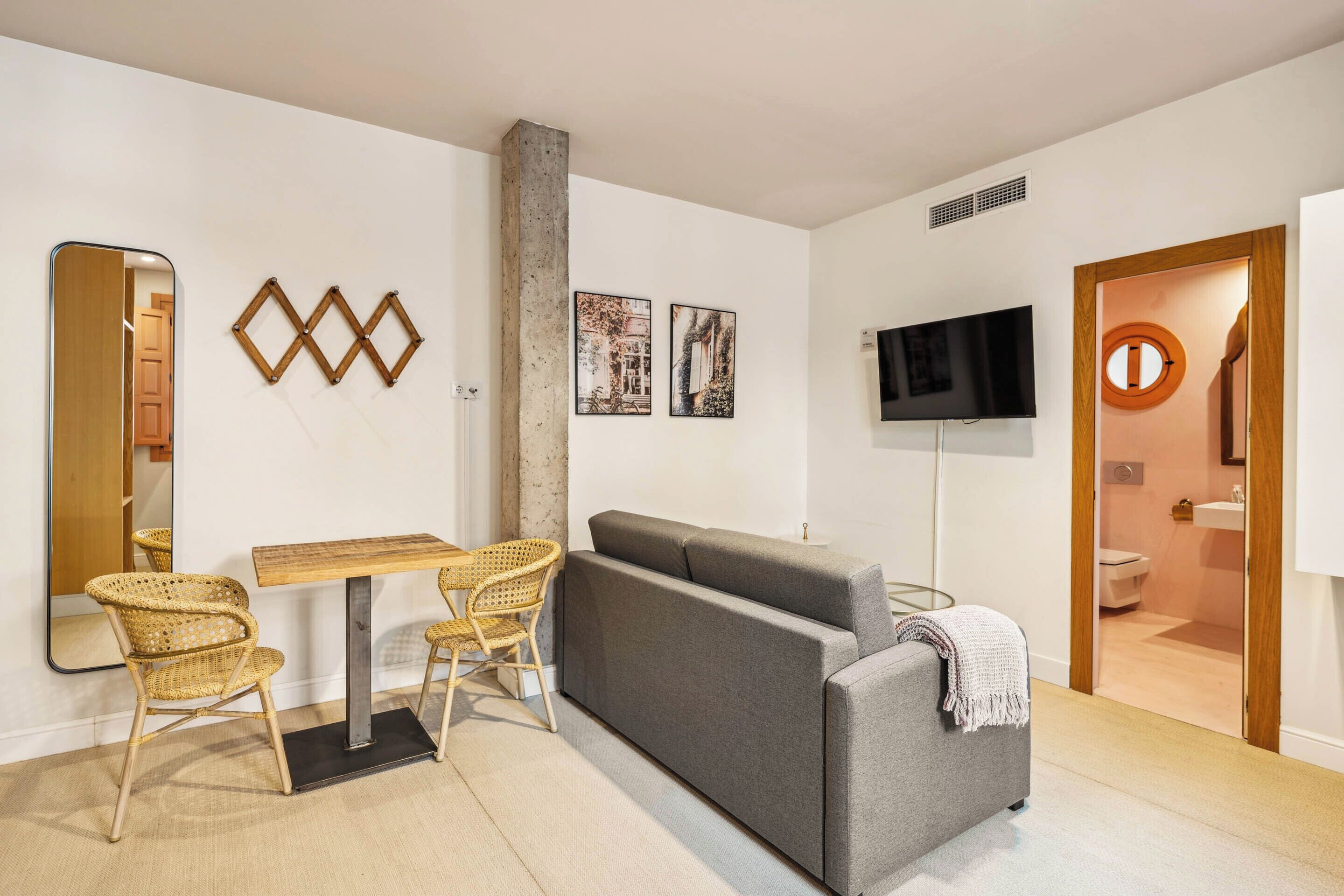 Una sala de estar moderna con un sofá gris, sillas de mimbre, una mesa de madera, un televisor de pantalla plana y obras de arte en las paredes.