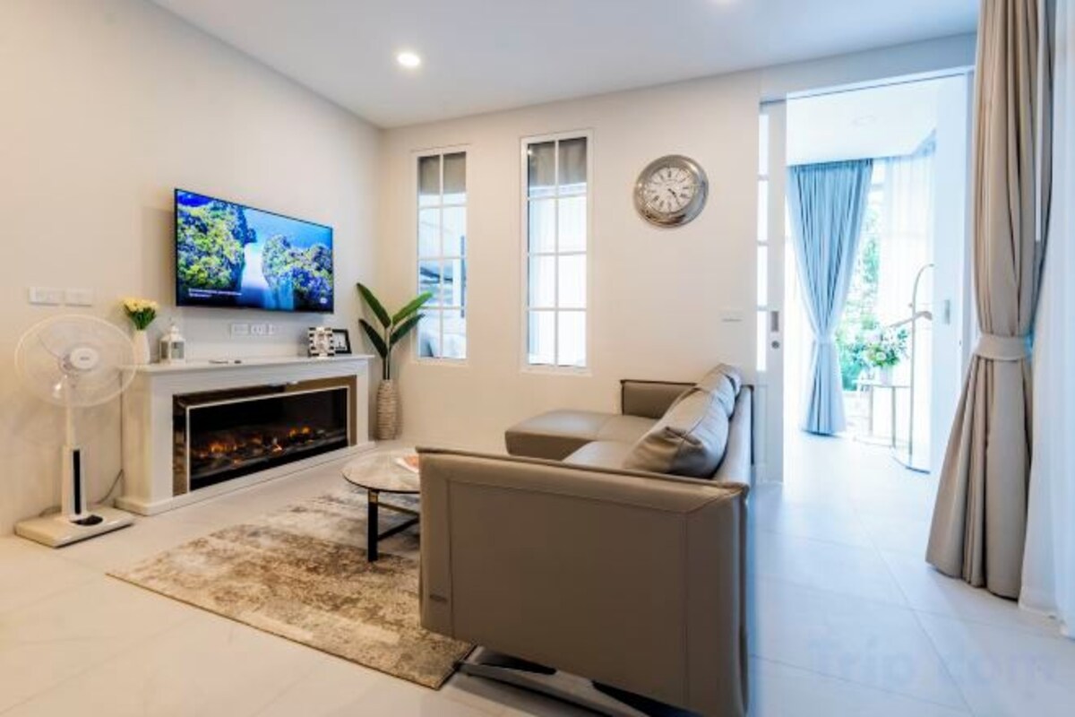 A modern living room with a flat-screen TV, a fireplace, a sofa, and a large window.
