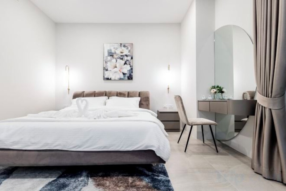 A modern bedroom with a large bed, bedside table, and a mirror.