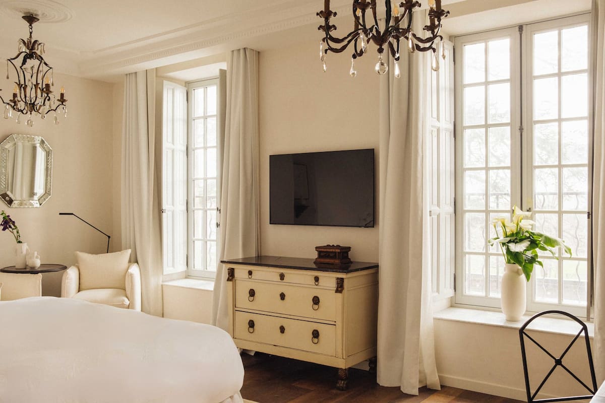 Een slaapkamer met een groot bed, een dressoir, een televisie en een raam met gordijnen.