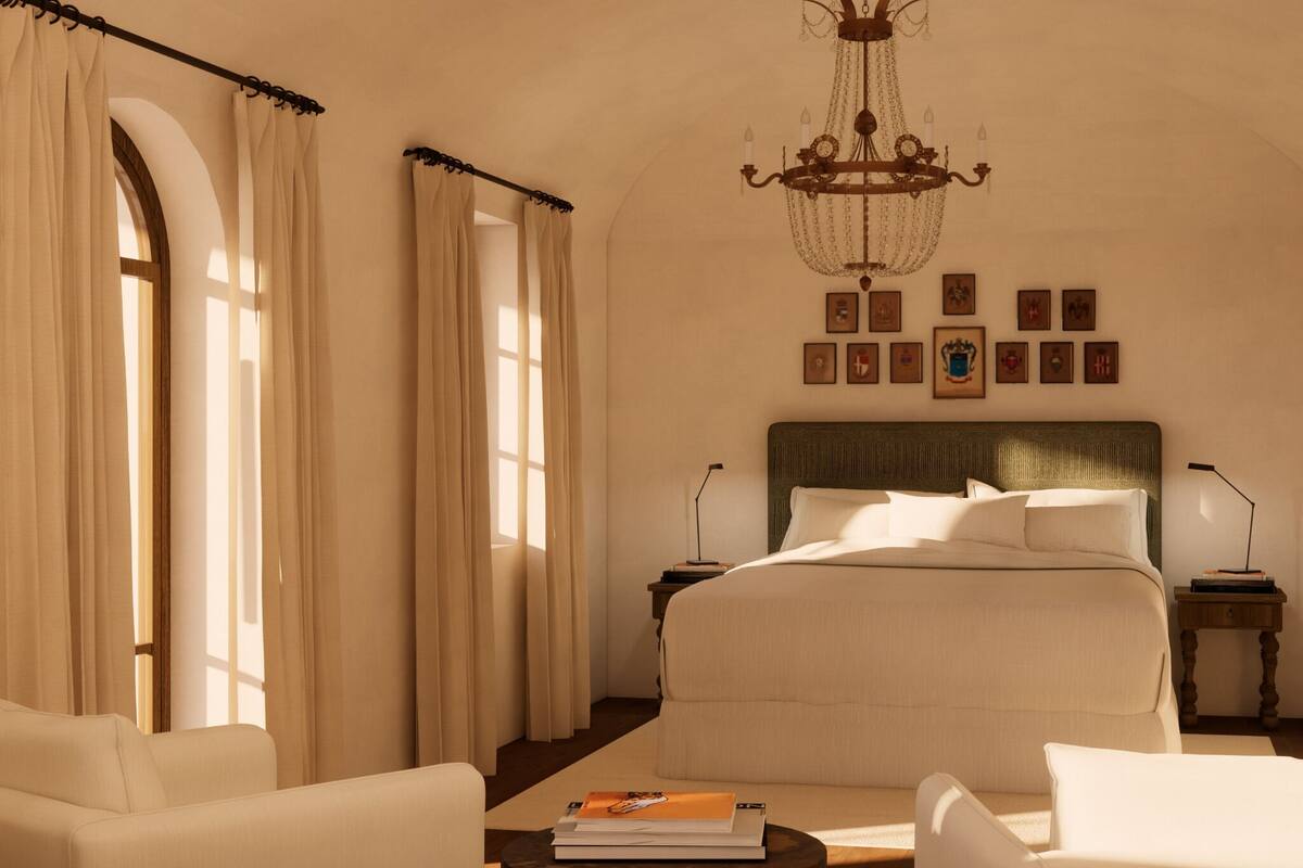 Een slaapkamer met een groot bed, twee nachtkastjes, een kroonluchter en uitzicht buiten door een raam met gordijnen.