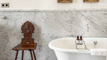 A bathroom with a marble floor, a white bathtub, a wooden chair, and two framed pictures on the wall.
