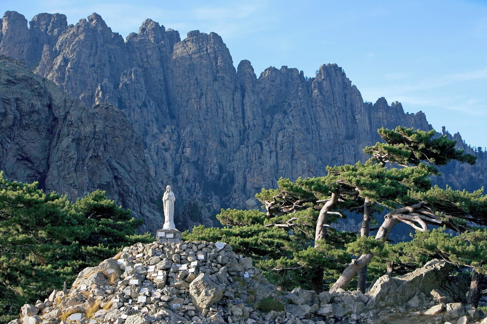 A rocky monument with a statue in front of a mountain range.