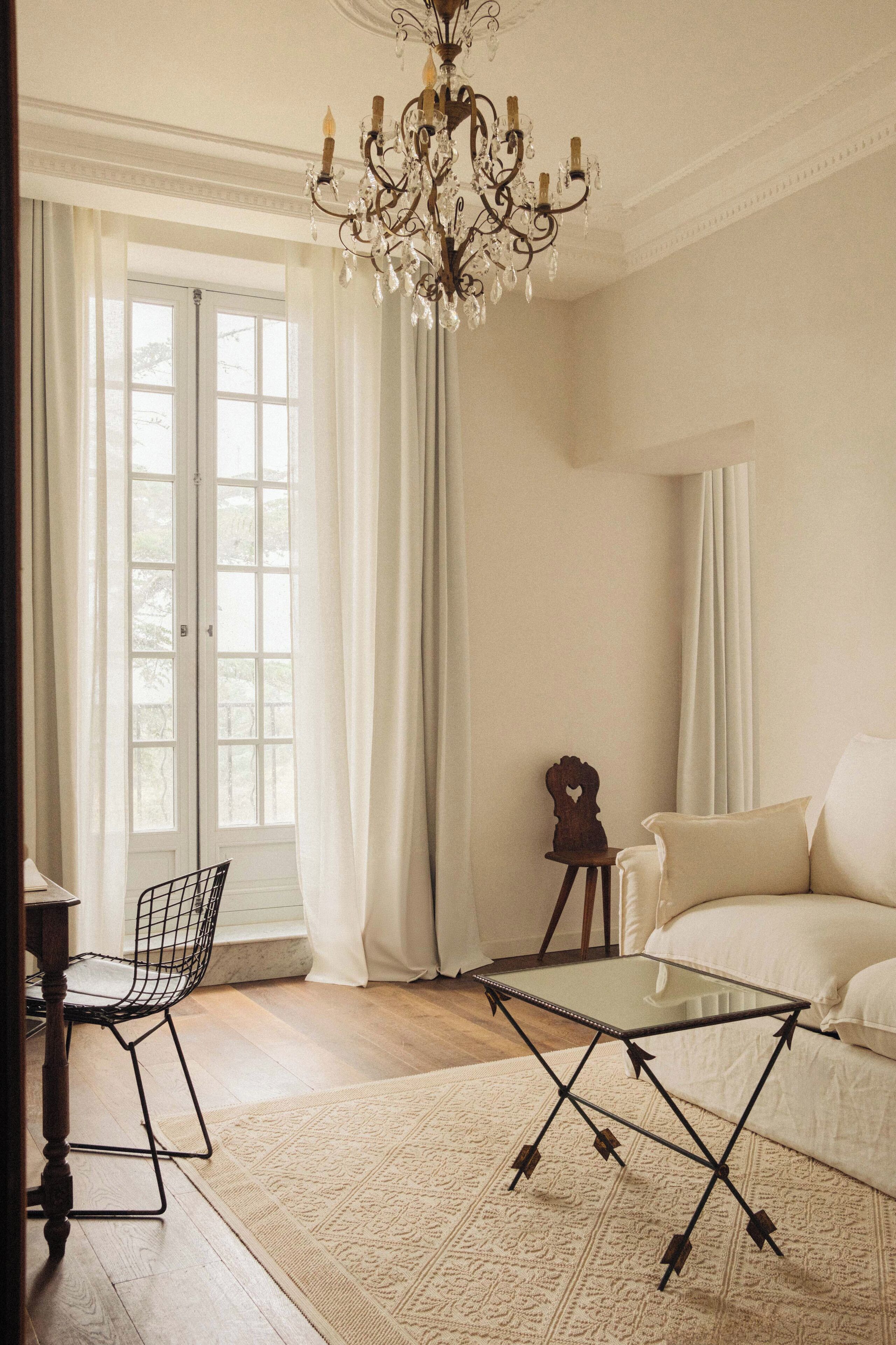 A room with a chandelier, a glass-top table, a sofa, and a chair.