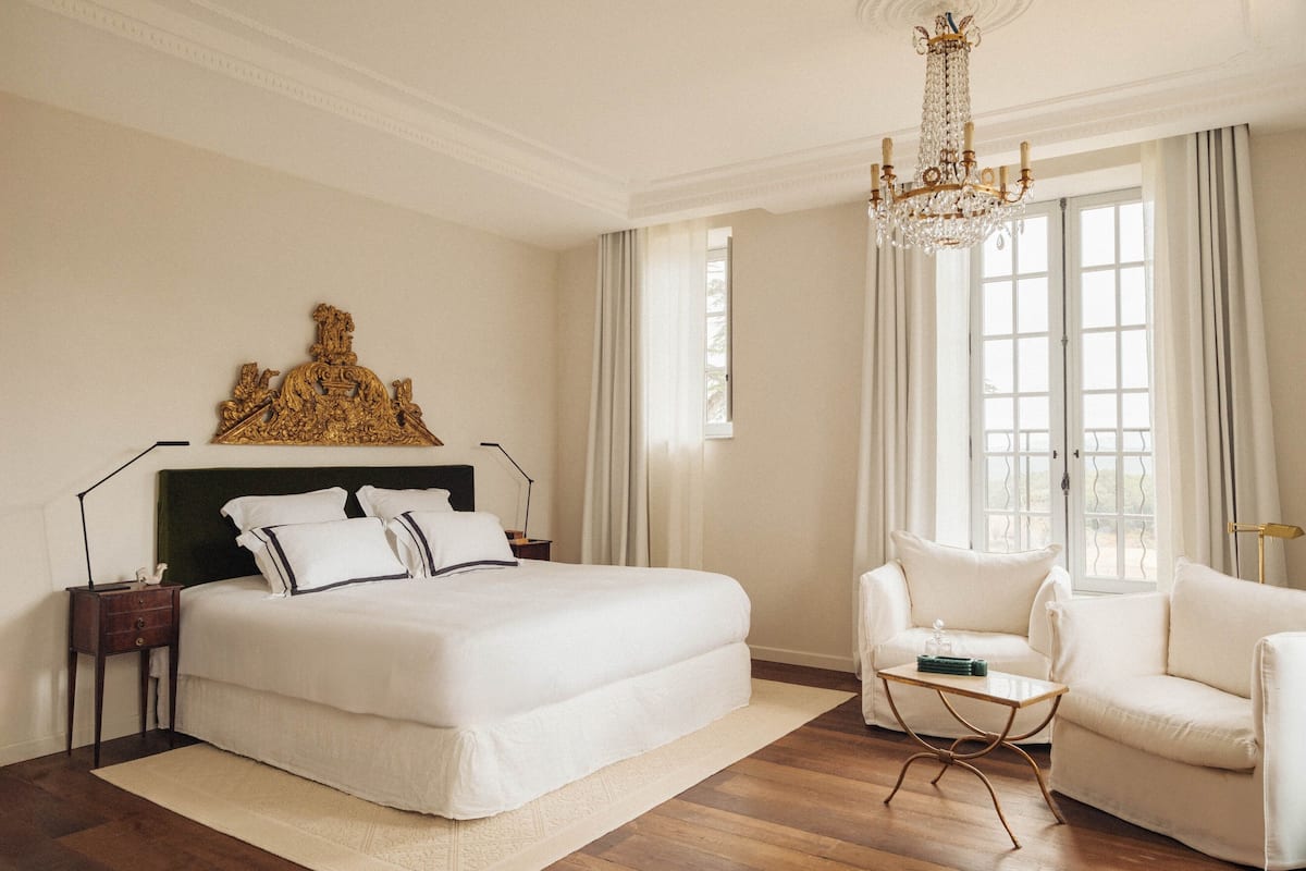 Een ruime slaapkamer met een groot bed, een kroonluchter, een sofa en een decoratief wandobject.