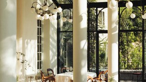 An indoor dining area with tables set for two, white columns, and hanging light fixtures.