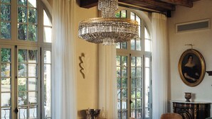 A room with large windows, a chandelier, and vintage furniture.