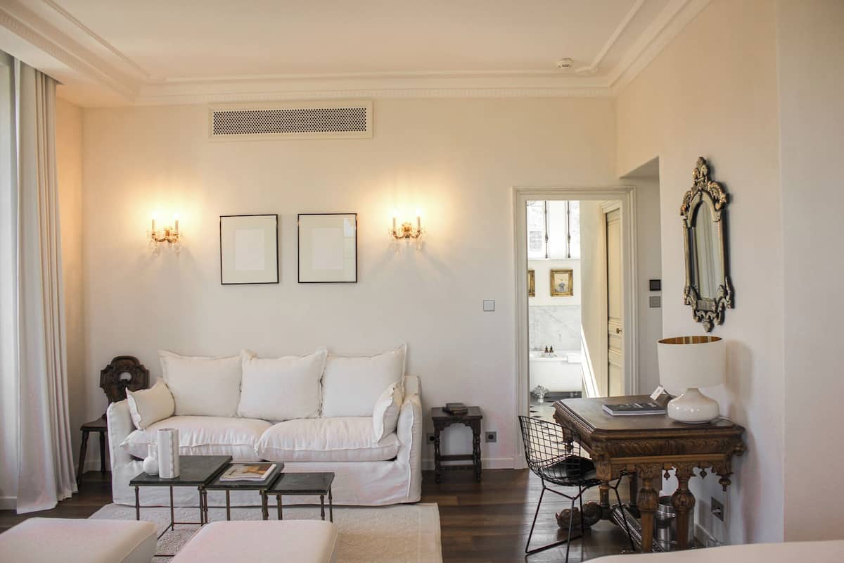 Een woonkamer met een witte bank, een salontafel en een lamp op een bijzettafeltje. Twee wandlampen en een spiegel sieren de muur.