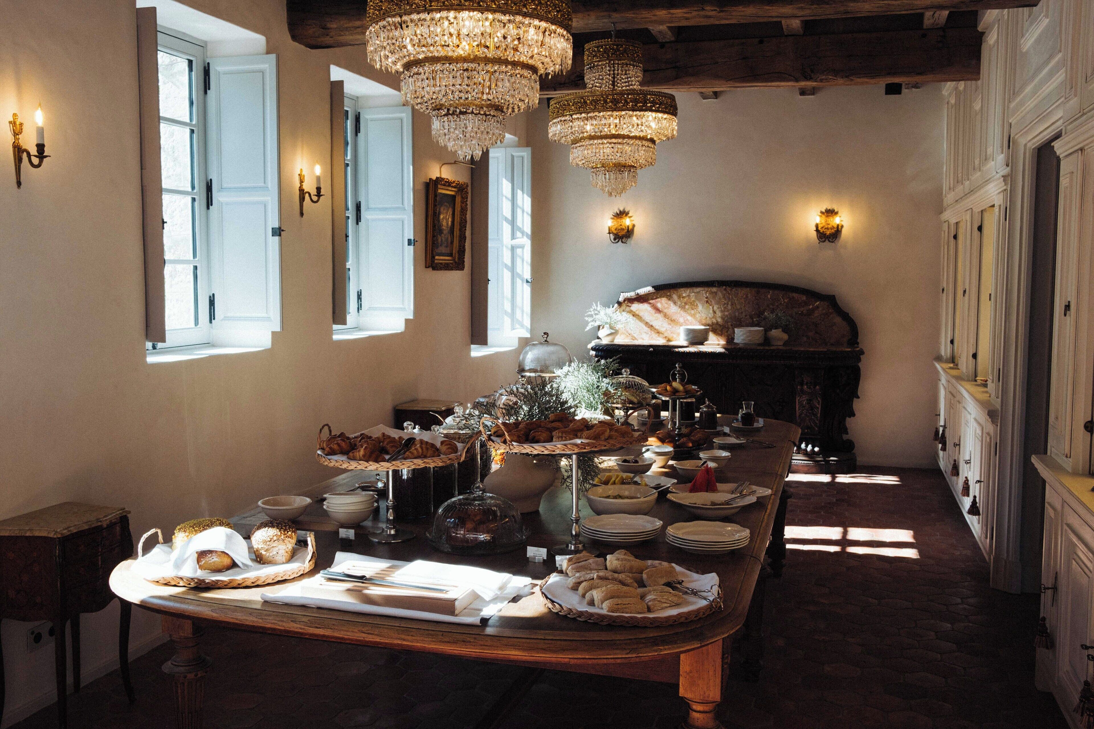 Une salle à manger avec une longue table dressée pour un repas, des lustres et une cheminée en arrière-plan.