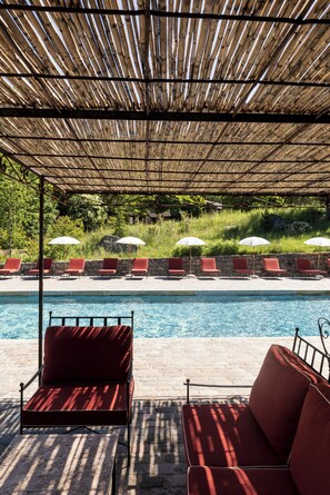 A poolside area with a covered seating area, lounge chairs, and umbrellas.